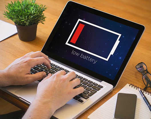 A Person Working on his Laptop with Battery Low Screen